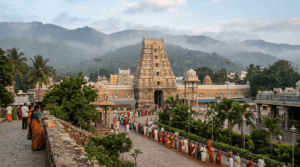 A respectful exterior image of Tirumala temple with pilgrims and hills in the background.