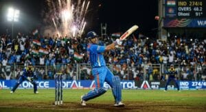 MS Dhoni in blue Indian cricket jersey playing the helicopter shot at a packed floodlit stadium during the 2011 World Cup final